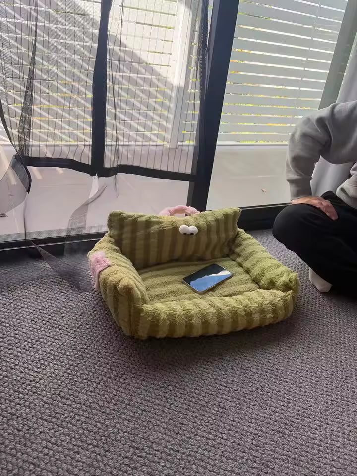 Green pet bed on a gray carpet with a person sitting nearby.