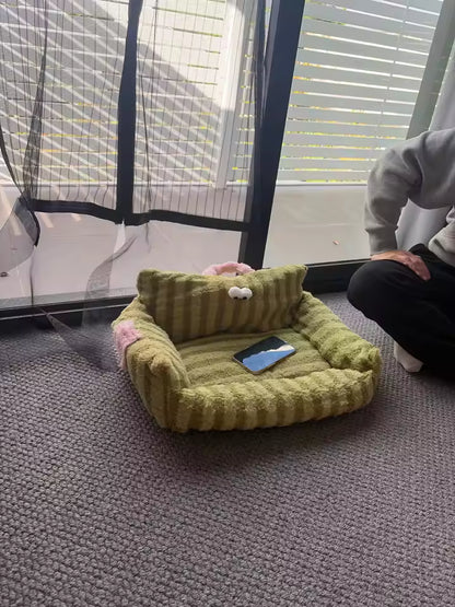 Green pet bed on a gray carpet with a person sitting nearby.